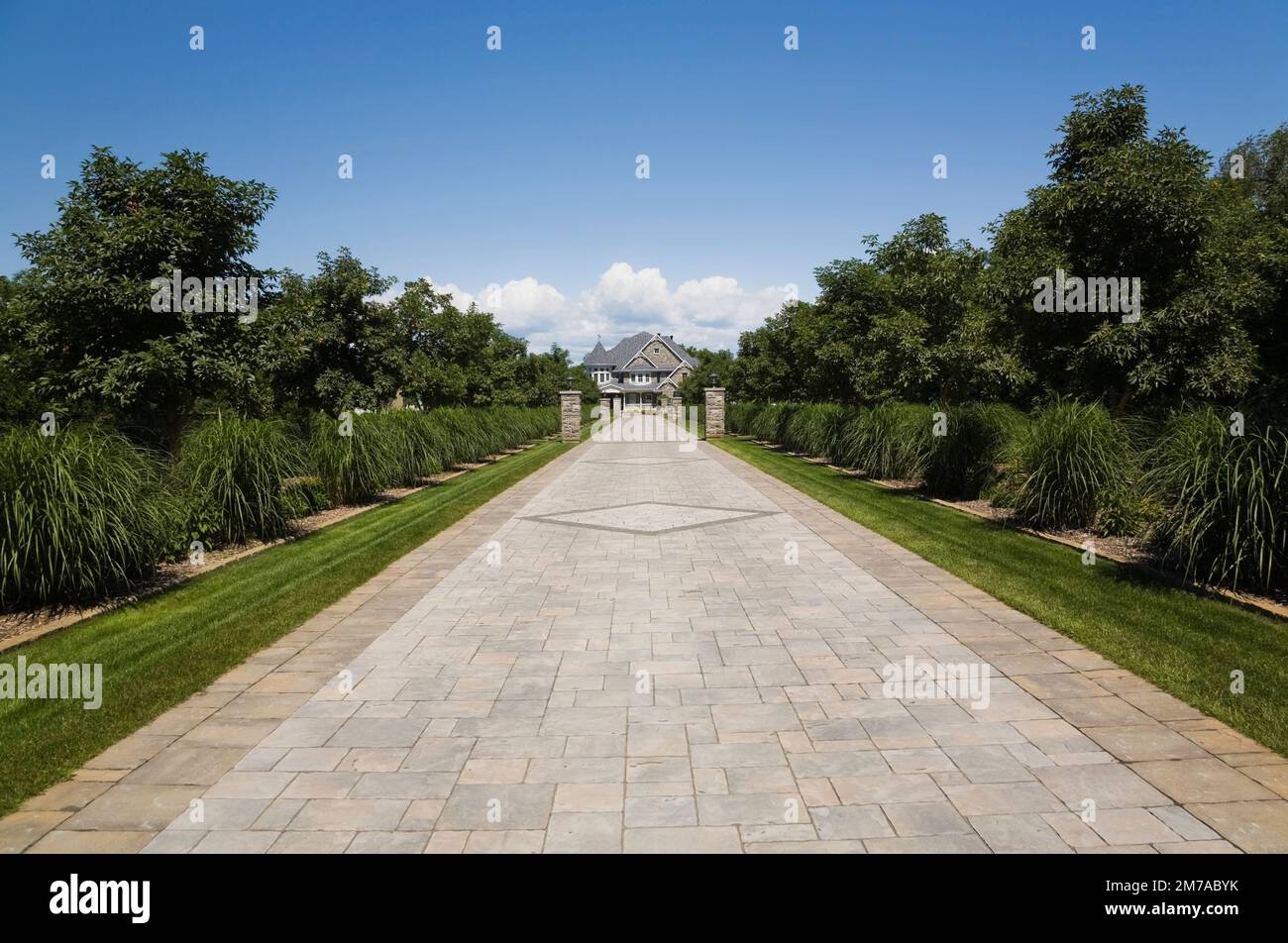 Vicolo in pietra con colonne in pietra delimitate da Miscanthus - piante ornamentali che conducono a un'elegante pietra grigia con finiture bianche e tetto blu. Foto Stock