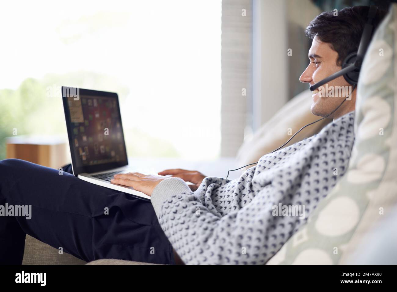 Navigare, parlare e ascoltare, che dice gli uomini cant multitasking. un giovane uomo che indossa un auricolare mentre usa il computer portatile a casa. Foto Stock