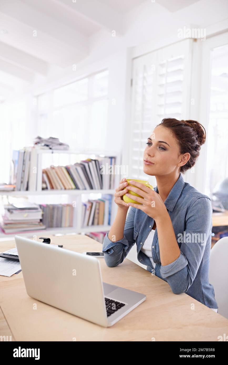 Contempla la giornata davanti a una tazza di caffè appena fatto. una donna attraente che usa il suo notebook a casa. Foto Stock