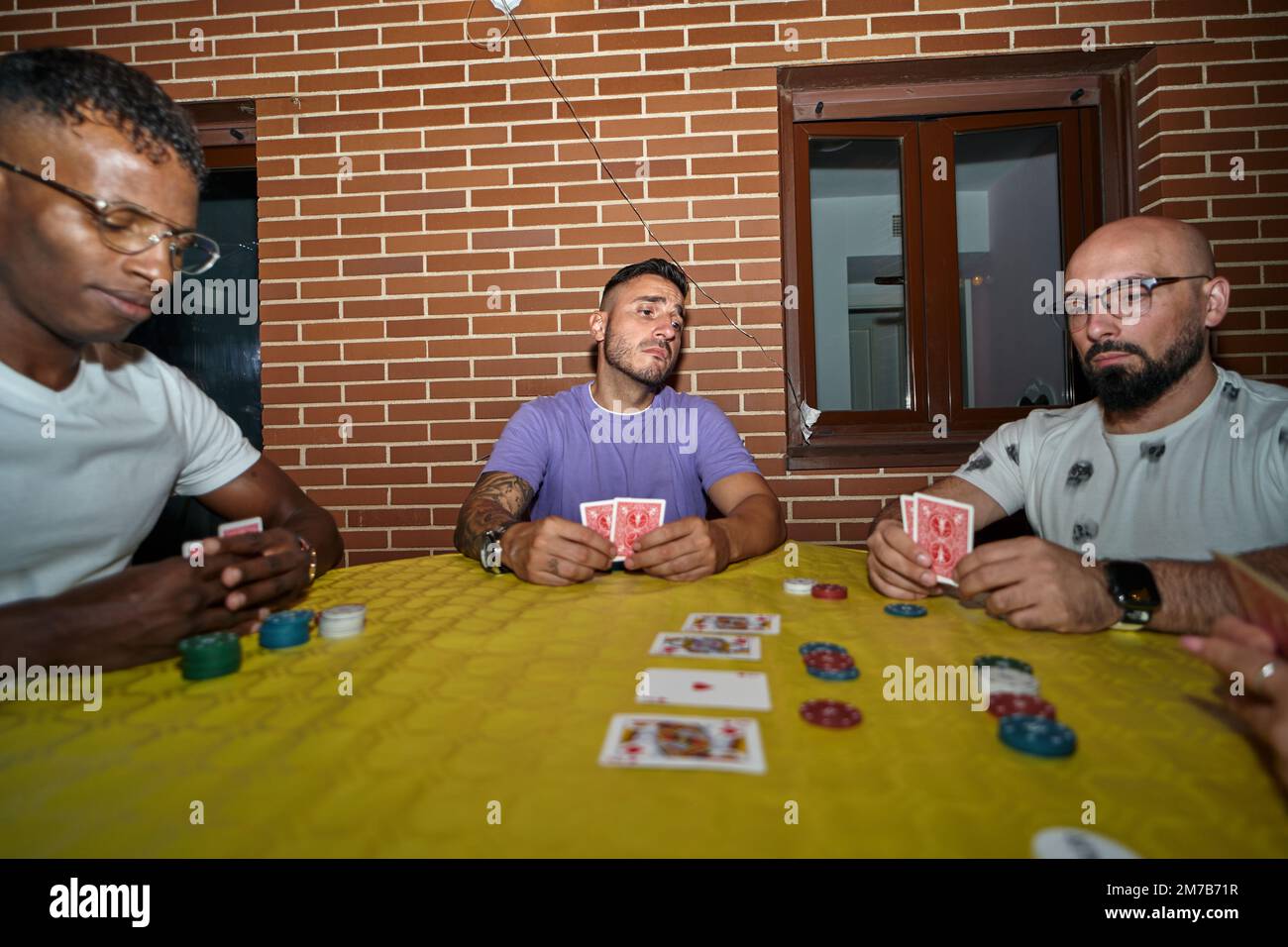 Amici maschi che giocano a poker mentre si siedono su un tavolo all'aperto in una terrazza. Foto Stock
