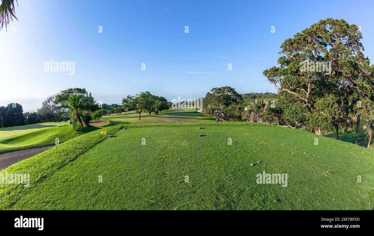 Campo da golf disposizione panoramica del design costiero tee box fairway putting green circondato da alberi vegetazione estate blu cielo paesaggio. Foto Stock