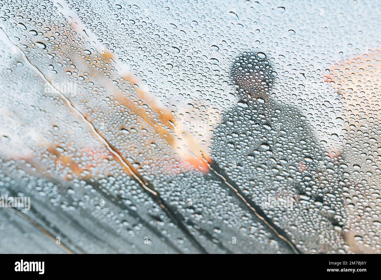 Autolavaggio uomo con pistola ad acqua in autolavaggio self-service. Sapone, cera e gocce d'acqua che coprono il cristallo del finestrino del veicolo. Visto dall'interno dell'autom Foto Stock