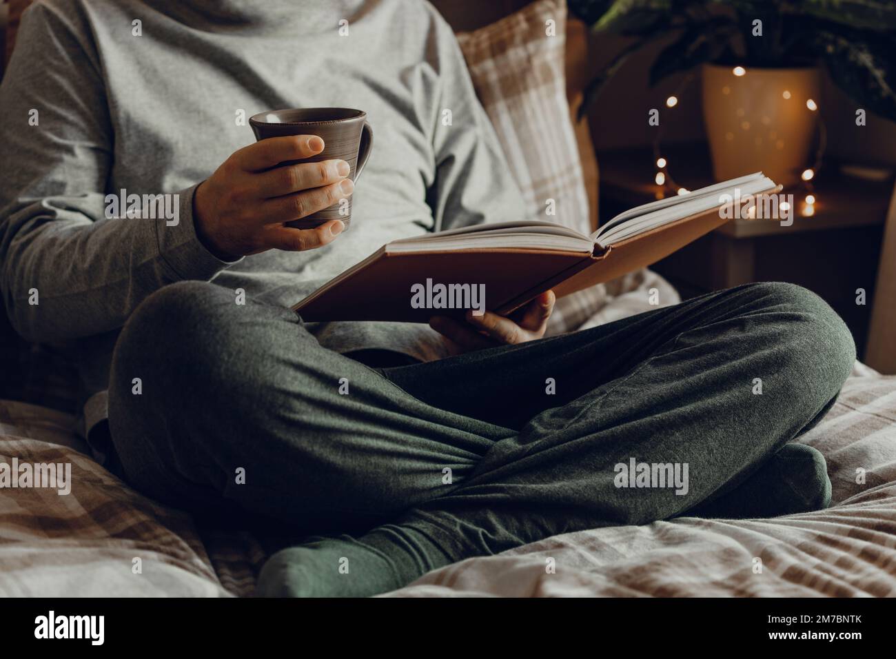 Un uomo caucasico che si rilassa a casa, leggendo un libro, bevendo caffè a letto Foto Stock