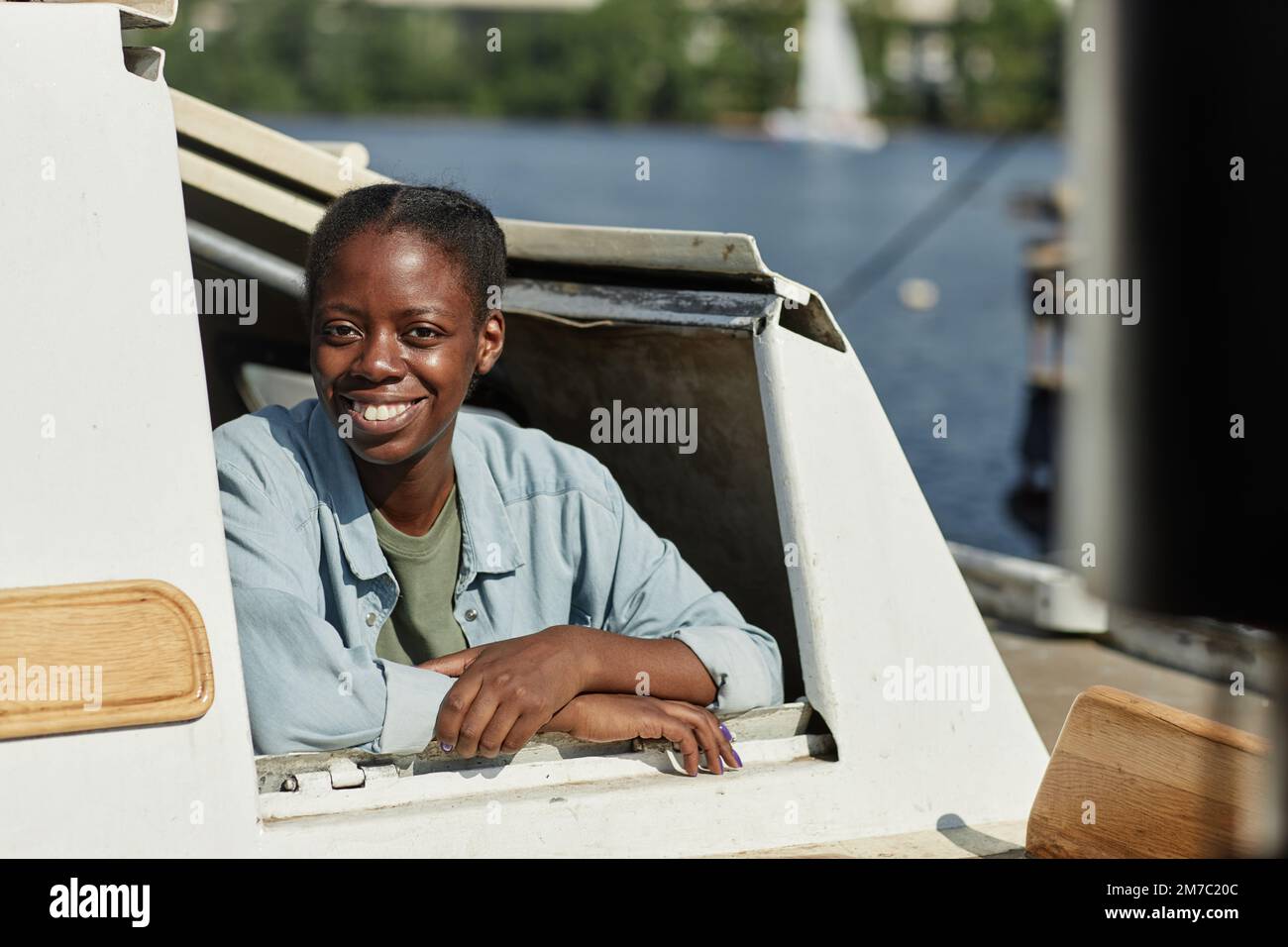 Ritratto di giovane donna nera sorridente alla fotocamera mentre si guarda fuori barca finestra, copia spazio Foto Stock