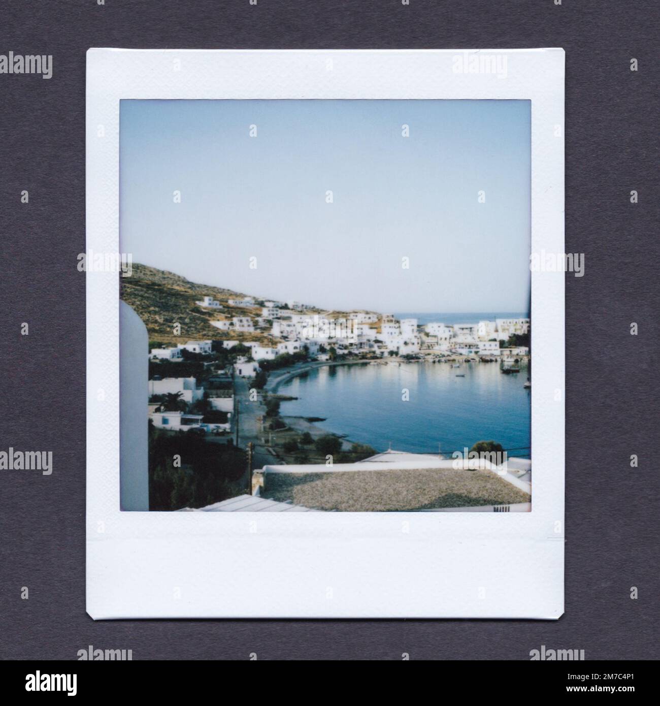 Stampa INSTAX su sfondo grigio scuro, con il porto di Folegandros, con edifici bianchi intorno all'acqua. Foto Stock