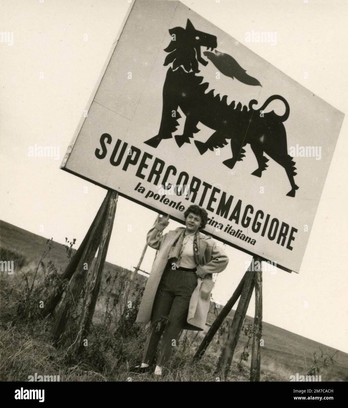 Donna in posa sotto il cartellone Supercortemaggiore benzina pubblicità, Italia 1960s Foto Stock