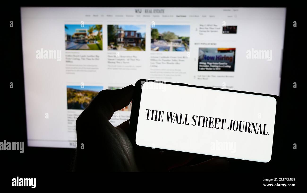 Persona che tiene il cellulare con il logo del giornale degli Stati Uniti il Wall Street Journal sullo schermo di fronte alla pagina web. Messa a fuoco sul display del telefono. Foto Stock