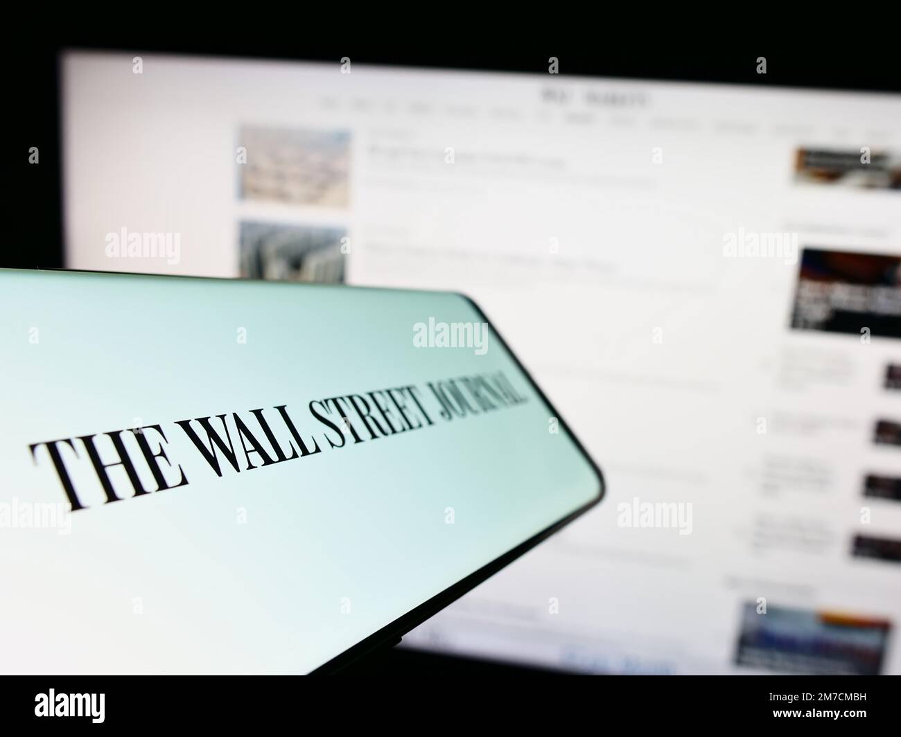 Smartphone con il logo del giornale americano The Wall Street Journal sullo schermo di fronte al sito Web. Messa a fuoco al centro a sinistra del display del telefono. Foto Stock