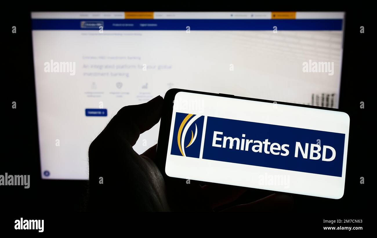 Persona che detiene il telefono cellulare con il logo della società finanziaria Emirates NBD Bank PJSC sullo schermo di fronte alla pagina Web aziendale. Messa a fuoco sul display del telefono. Foto Stock