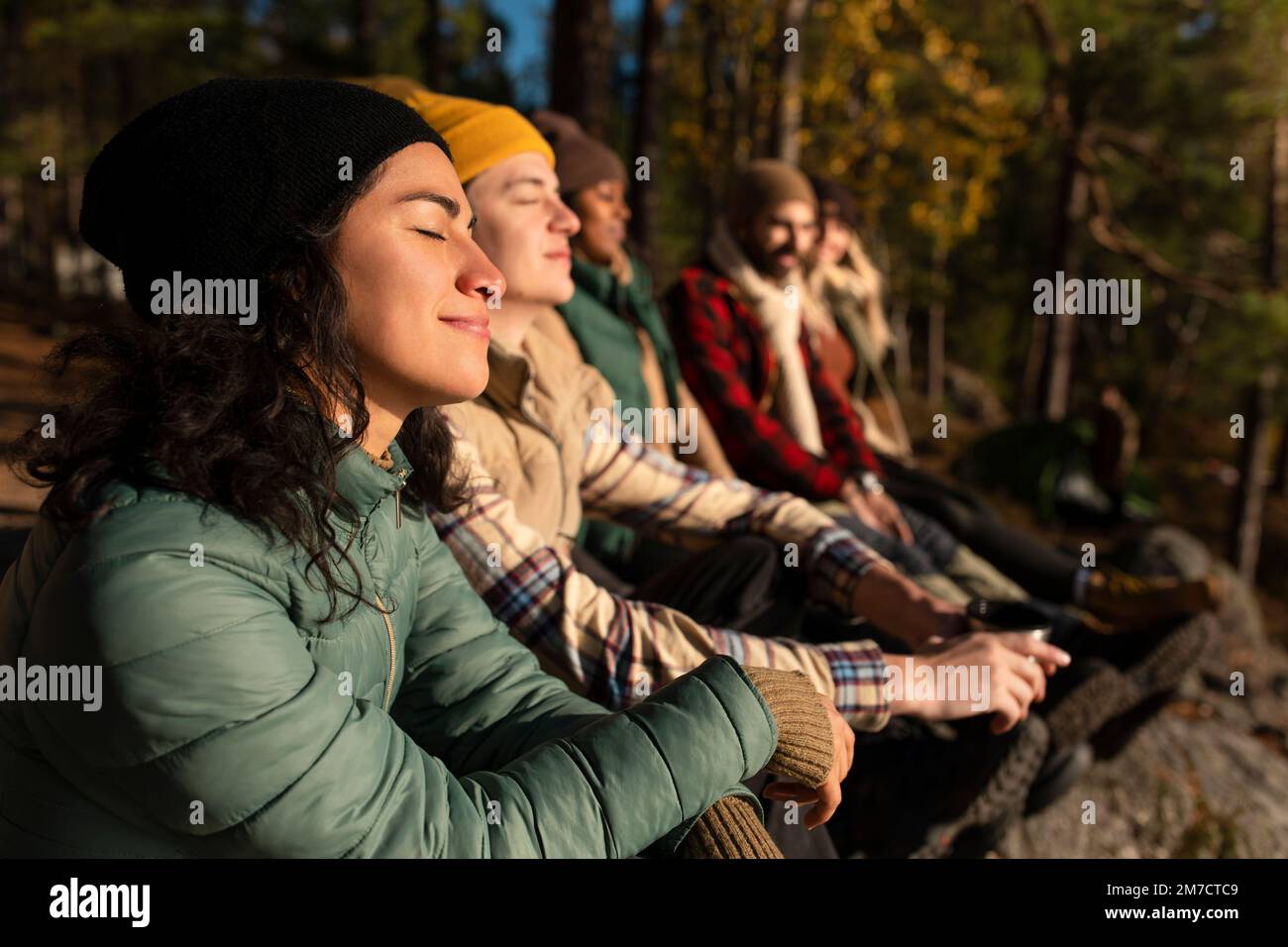 Vista laterale di una donna sorridente con gli occhi chiusi godendosi la luce del sole mentre si siede da amici nella foresta Foto Stock