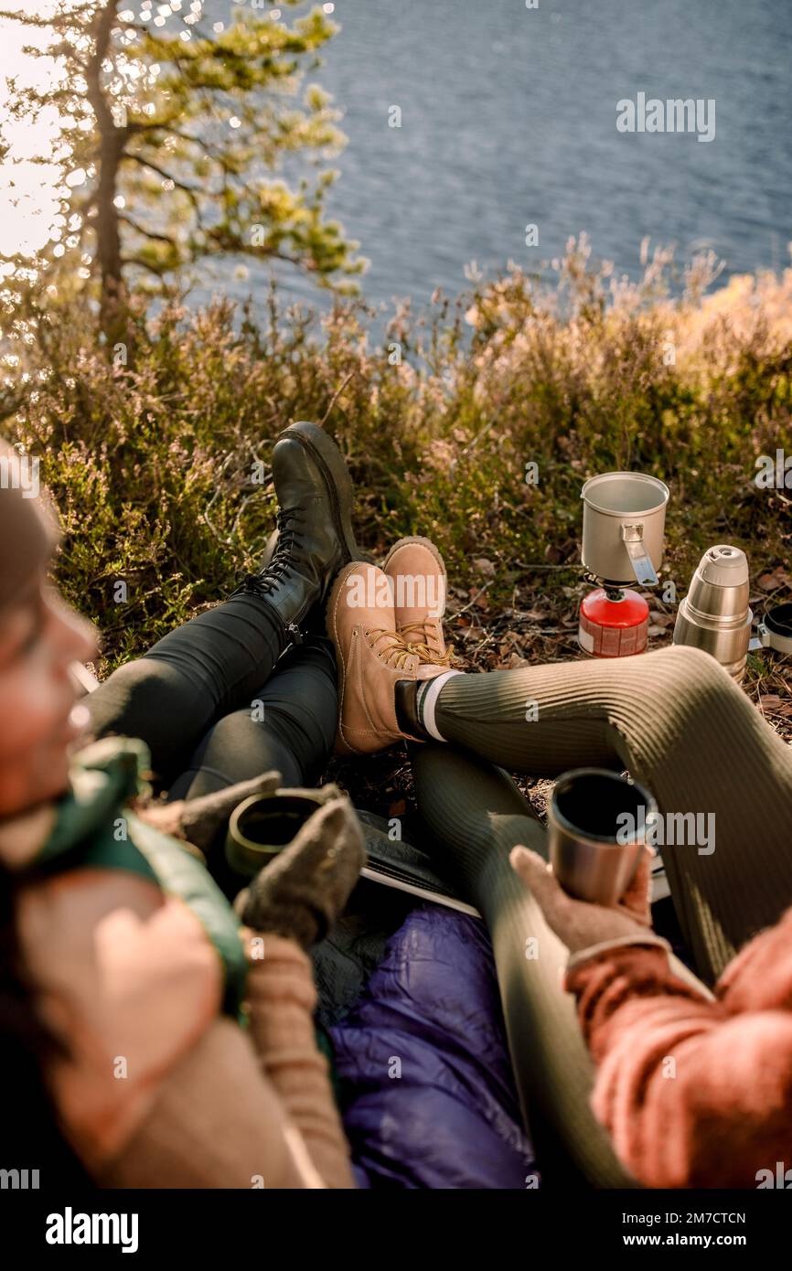 Vista ad alto angolo degli amici che indossano stivali mentre si siedono sull'erba durante il campeggio Foto Stock