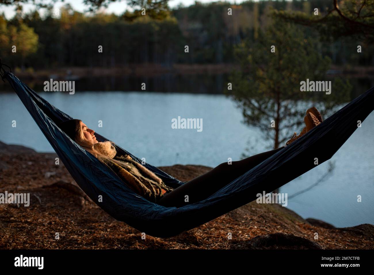Giovane donna che dorme su amaca al lago durante il tramonto Foto Stock