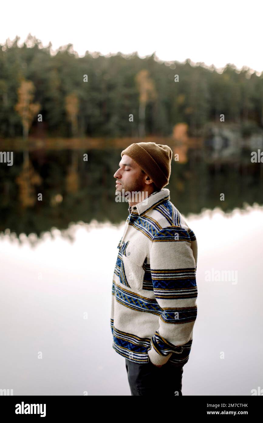 Vista laterale dell'uomo con mano in tasca in piedi vicino al lago Foto Stock