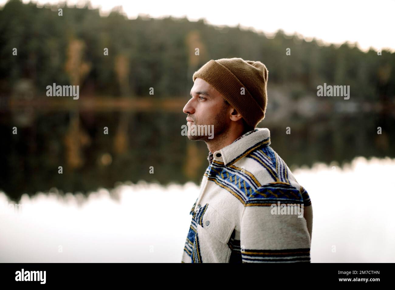 Uomo premuroso in maglia cappello in piedi accanto al lago Foto Stock