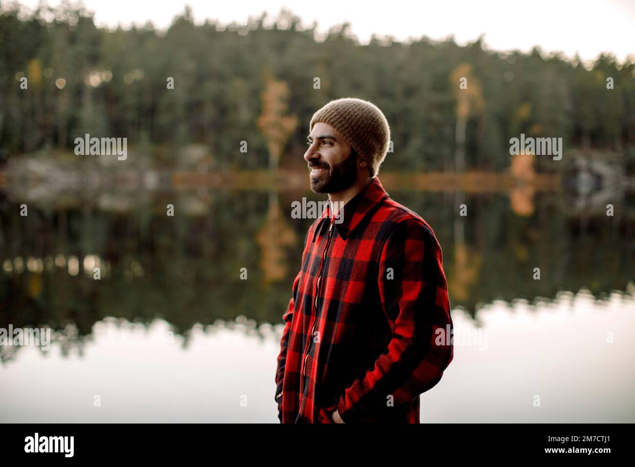 Uomo sorridente che indossa una maglietta a quadri mentre si trova vicino al lago Foto Stock