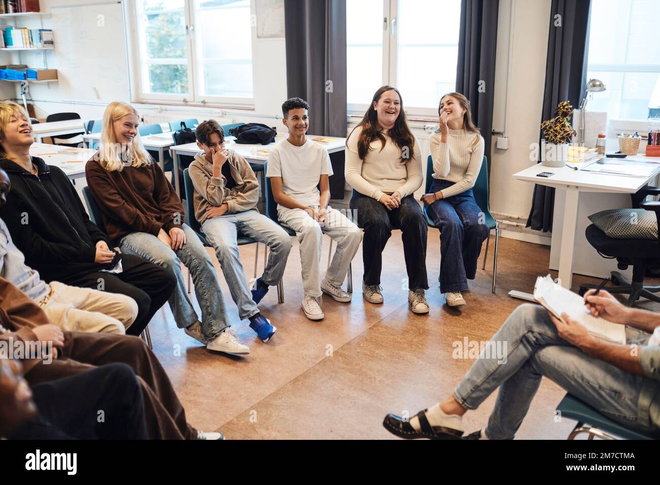 Felici studenti maschi e femmine seduti con un consulente in terapia di gruppo a scuola Foto Stock