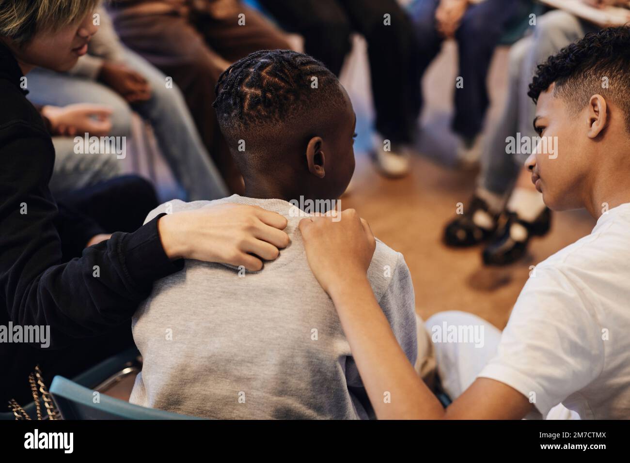 Ragazzi multirazziali che consolano un amico maschio con le braccia intorno in terapia di gruppo a scuola Foto Stock