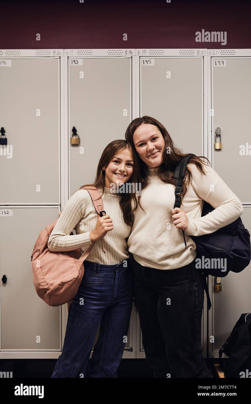 Ritratto di ragazze sorridenti con zaini in piedi contro armadietto a scuola Foto Stock
