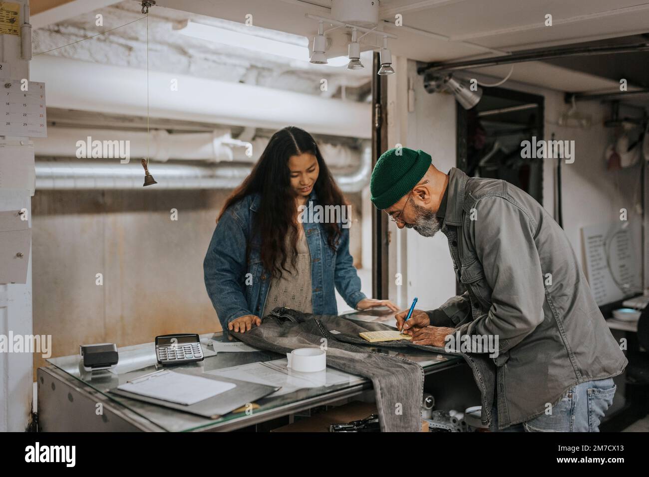 Uomo personalizzare la bolletta di scrittura mentre si è in piedi con il cliente al banco di lavoro Foto Stock