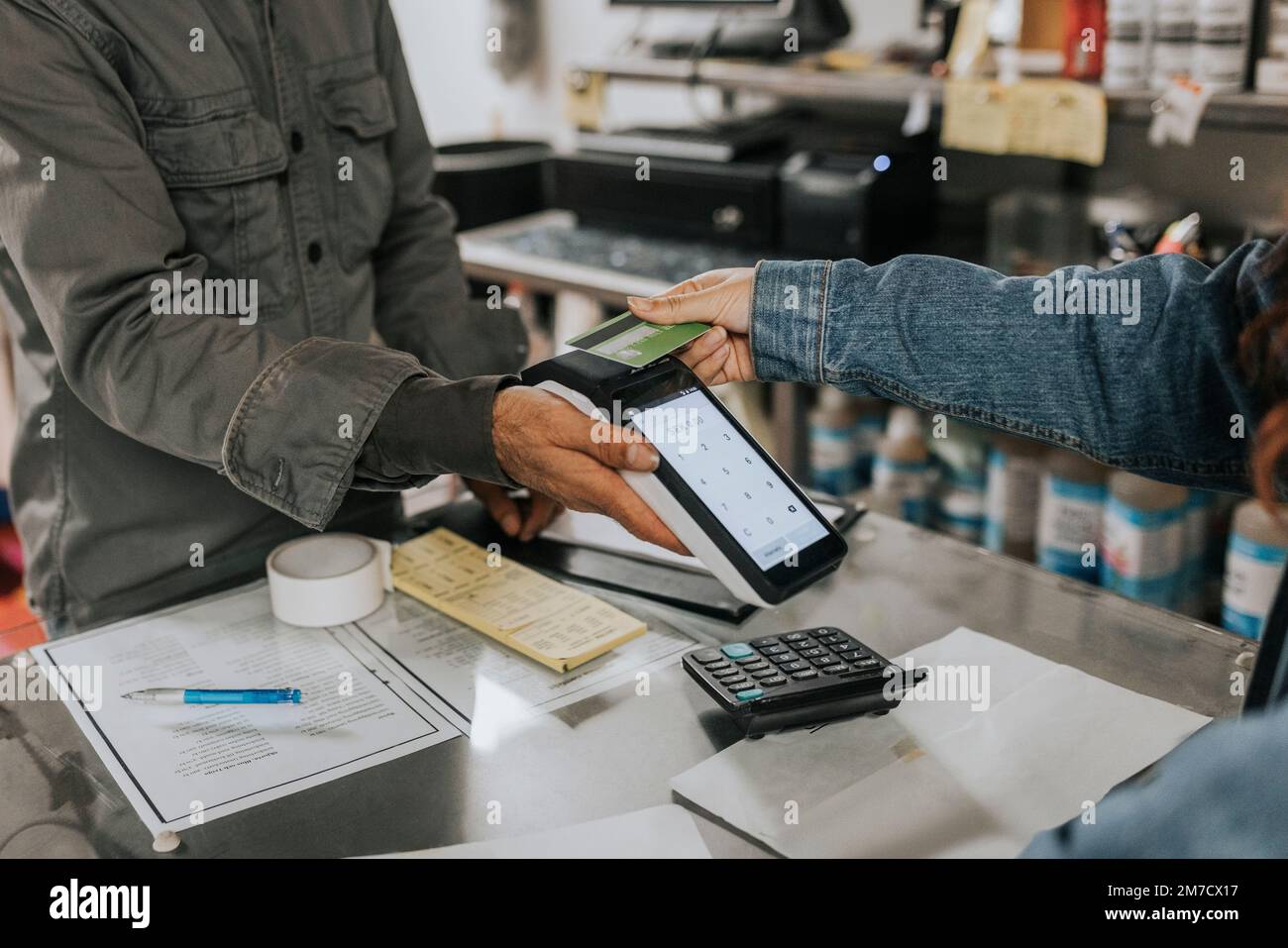 Maschio su misura tenendo lettore di carta di credito mentre il cliente femmina che effettua il pagamento contactless in officina Foto Stock