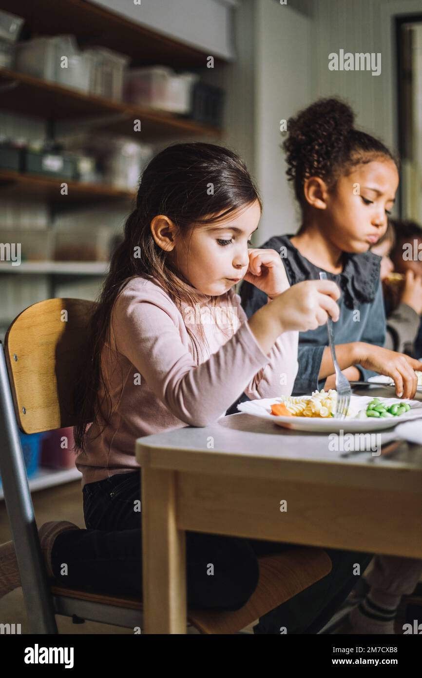 Ragazza che ha pasta per la prima colazione con una ragazza in classe nel centro di assistenza per bambini Foto Stock