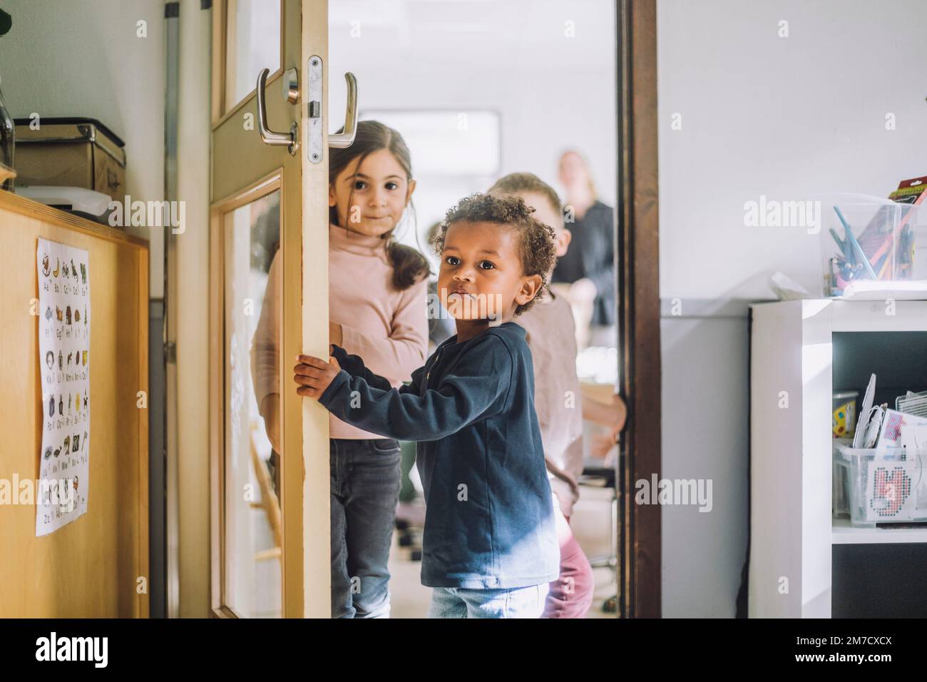 Ragazzo che apre la porta mentre si è in piedi con i compagni di classe alla porta dell'asilo Foto Stock