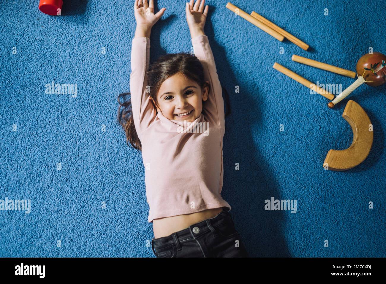 Ritratto di ragazza felice sdraiata su tappeto con giocattoli di legno nel centro di cura per bambini Foto Stock