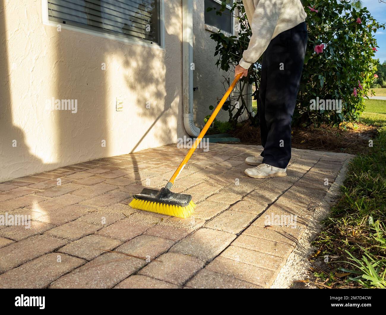 Uomo spazzante mattone finitrice portico in pietra con scopa a spinta. Foto Stock