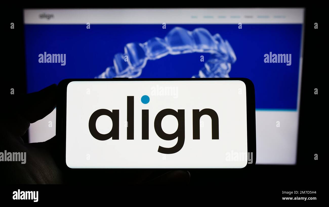 Persona che tiene il cellulare con il logo della società americana ortodonzia Align Technology Inc. Sullo schermo di fronte alla pagina web. Messa a fuoco sul display del telefono. Foto Stock