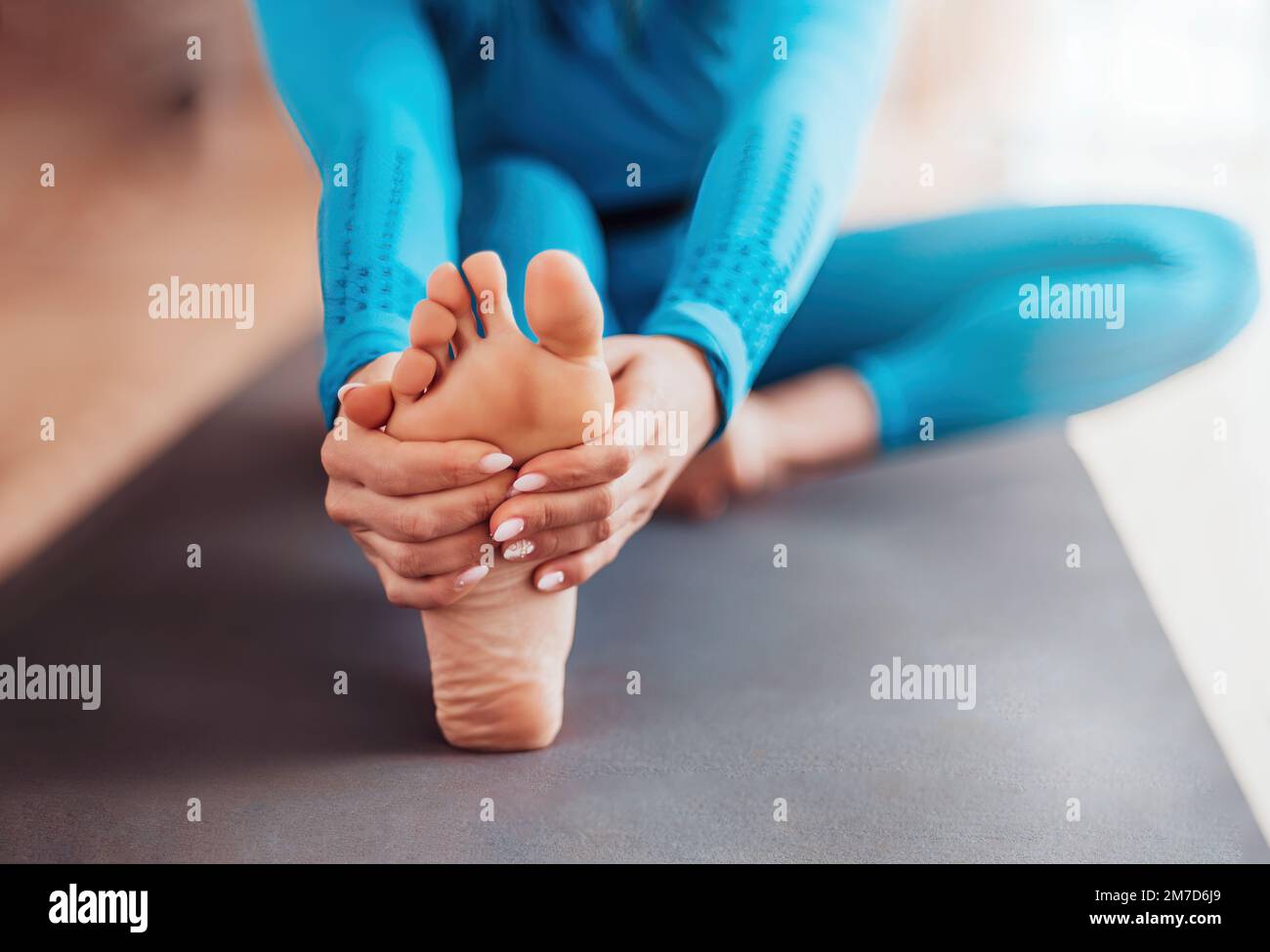 primo piano di piede e mani. sfocatura selettiva delle ragazze che si allungano prima di una lezione di yoga. indossa leggings blu. Foto Stock