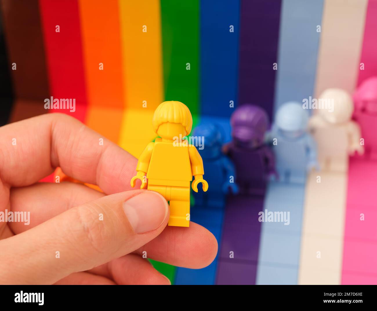 Tambov, Federazione Russa - 09 novembre 2022 Una mano donna che tiene una figura gialla Lego sopra altre figure arcobaleno. LEGO tutti sono fantastici Foto Stock