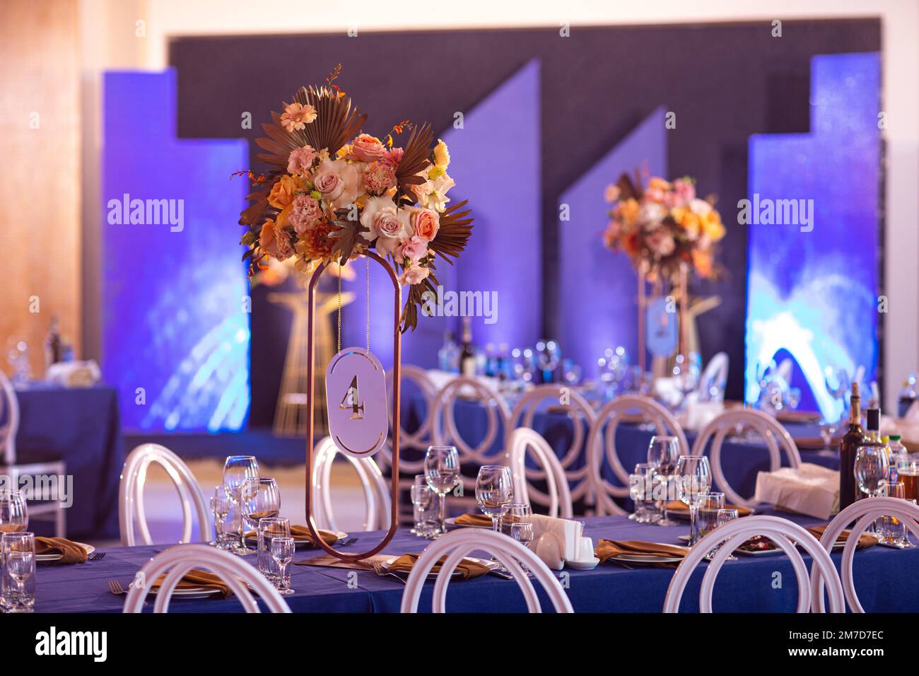 Tavolo festivo con stoffa blu, tovaglioli, piatti, posate e bicchieri preparati per gli ospiti del matrimonio nel ristorante. Bella composizione floreale in oro me Foto Stock