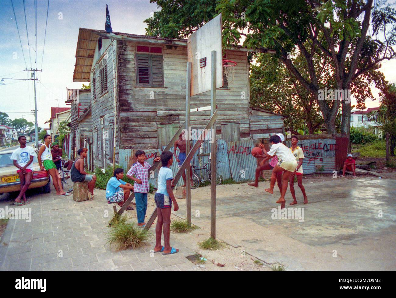 Surinam, i giovani sono appesi in giro per la strada a Paramaribo accanto a un'auto parcheggiata che è stato importato dall'ex sovrano coloniale olandese. Foto Stock