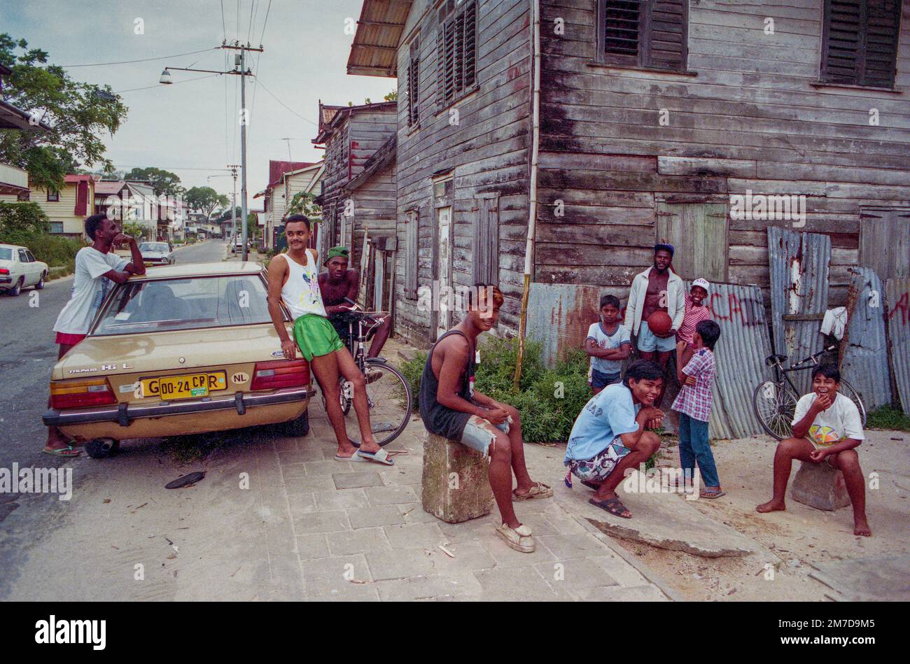 Surinam, i giovani sono appesi in giro per la strada a Paramaribo accanto a un'auto parcheggiata che è stato importato dall'ex sovrano coloniale olandese. Foto Stock