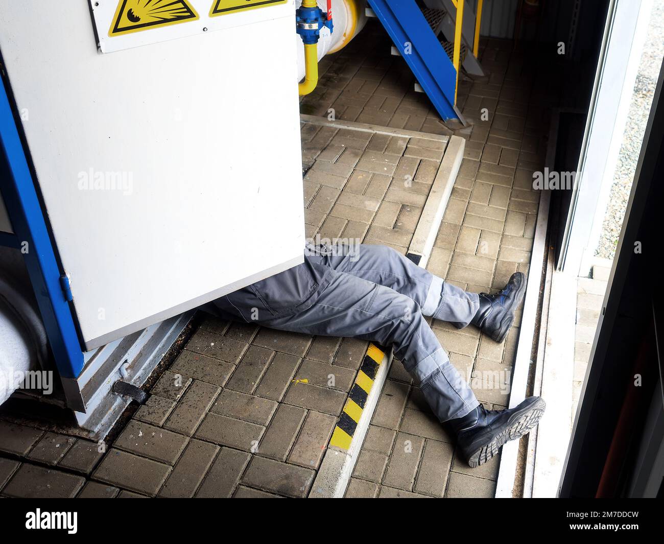 Incidente. Scossa elettrica a persona. Dal pannello elettrico, estrarre le gambe del lavoratore. L'elettricista è elettricizzato e si trova sul pavimento del sito di produzione. Rispetto della protezione del lavoro. Foto Stock