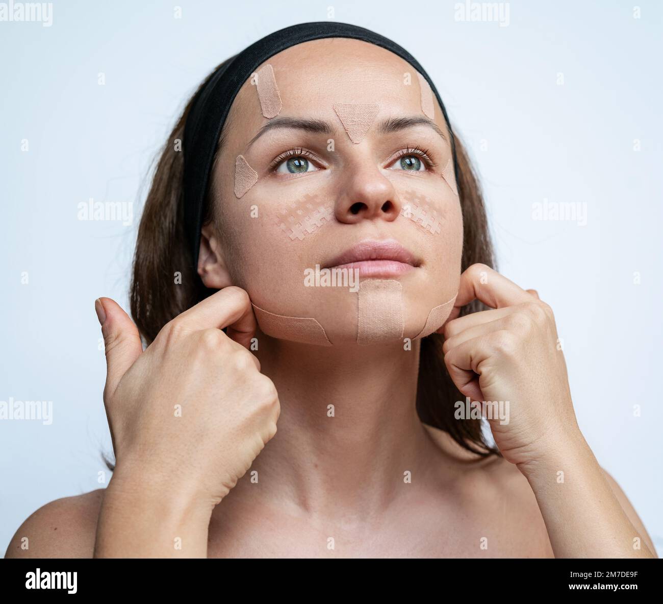 Donna attraente applicando nastro di cinesiologia facciale sul suo viso nastro facciale cura della pelle. Foto Stock