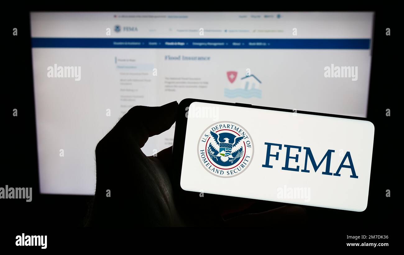 Persona che tiene il cellulare con sigillo della Federal Emergency Management Agency (FEMA) sullo schermo di fronte alla pagina web. Messa a fuoco sul display del telefono. Foto Stock Persona che tiene il cellulare con sigillo della Federal Emergency Management Agency (FEMA) sullo schermo di fronte alla pagina web. Messa a fuoco sul display del telefono. Foto Stock