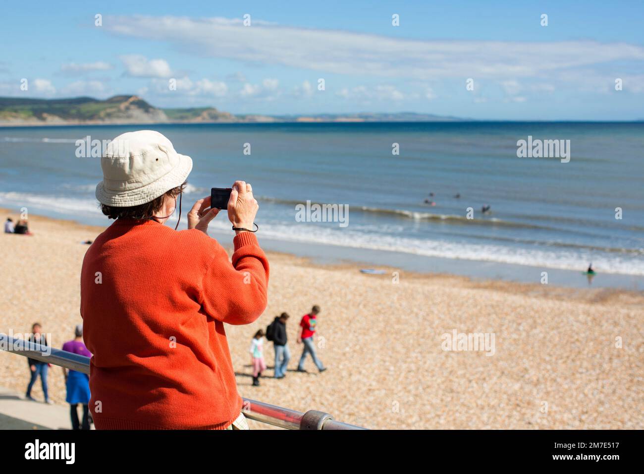 Un cappello non identificato indossando una donna che prende una foto della costa Dorset a Lyme Regis. Foto Stock
