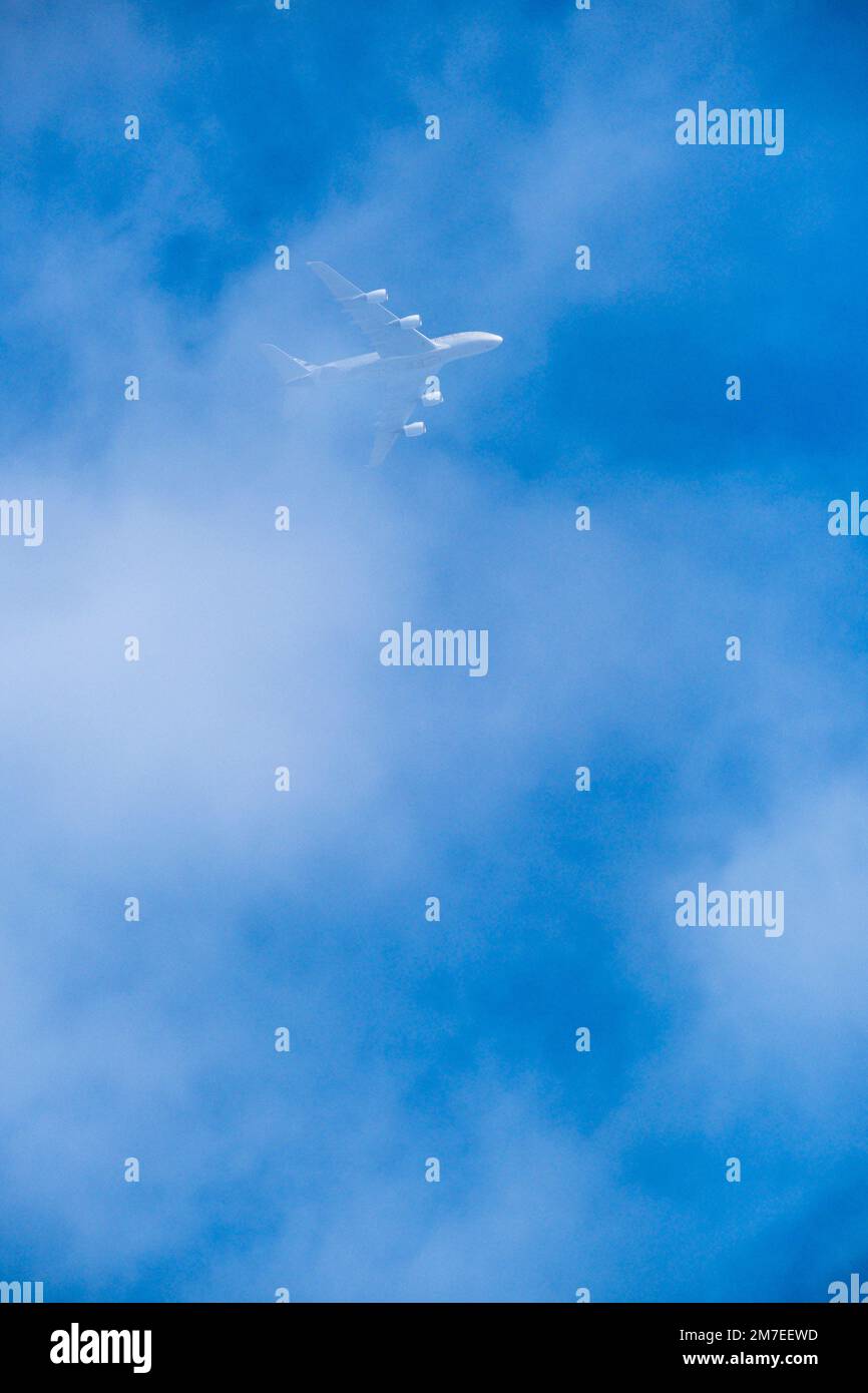 Un jet Aircraft passa sopra la testa attraverso la nuvola di luce che scompare dietro lo strato bianco posto contro un cielo blu. Foto Stock