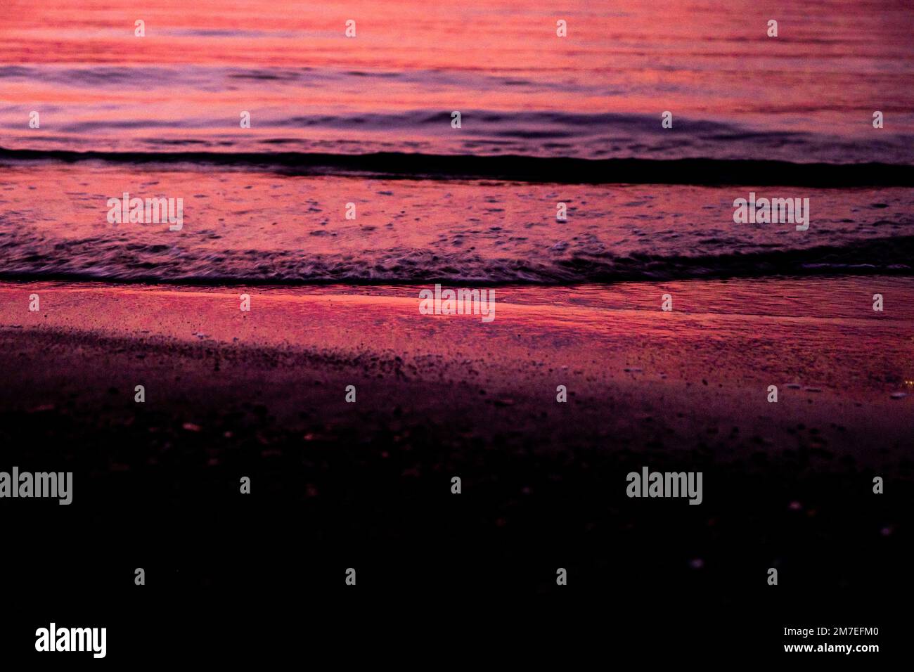 Piccole onde si adrotolano su una spiaggia di sabbia al tramonto con ondate sfocate e acqua ondulata. Foto Stock