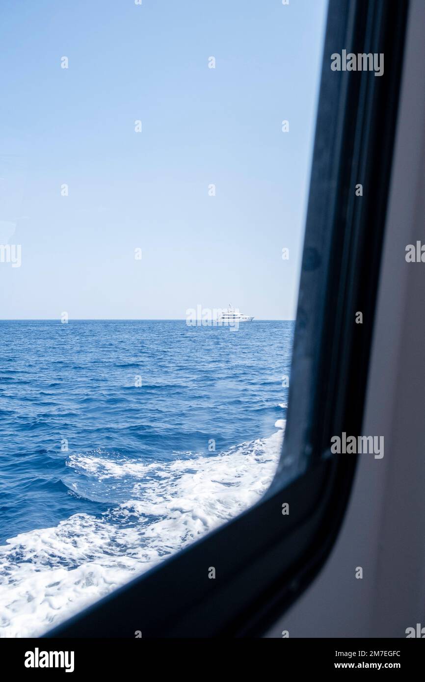 Guardando fuori dalla finestra di una barca turistica al mare con uno yacht a motore o più crudi in sella al rigonfiamento all'orizzonte. Foto Stock