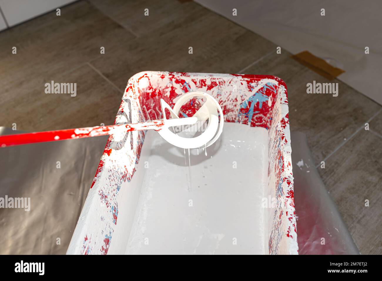 Un secchio di plastica aperto con vernice bianca e un agitatore in piedi sul pavimento. Foto Stock