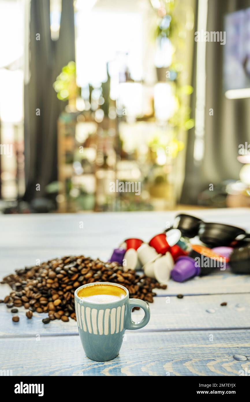 Una piccola tazza di caffè espresso in porcellana blu su un tavolo pieno di chicchi di caffè e cialde vicino alla finestra Foto Stock