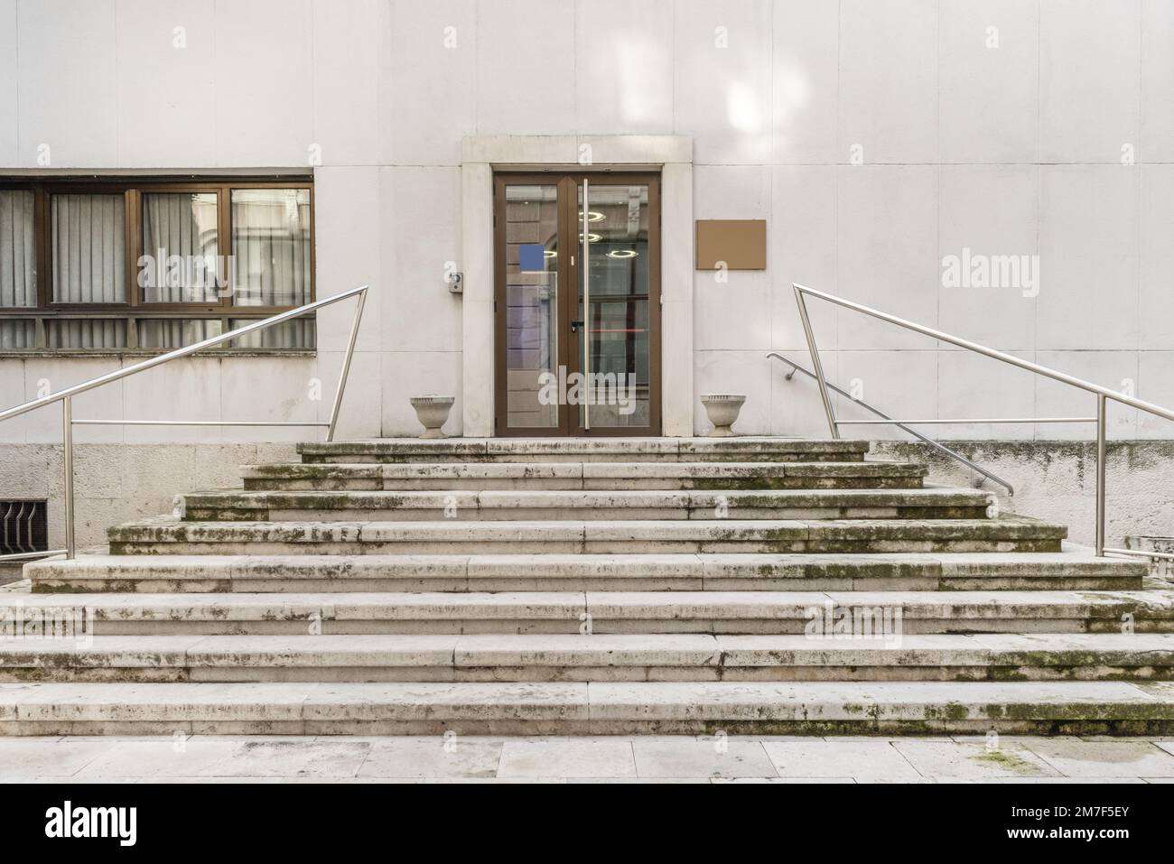 Scale in pietra che conducono ad un edificio con una facciata in marmo bianco e una porta in alluminio anodizzato marrone Foto Stock