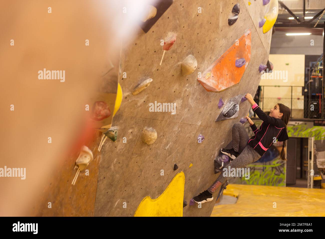 Piccola ragazza sportiva che arrampica masso artificiale sulla parete pratica dentro palestra Foto Stock