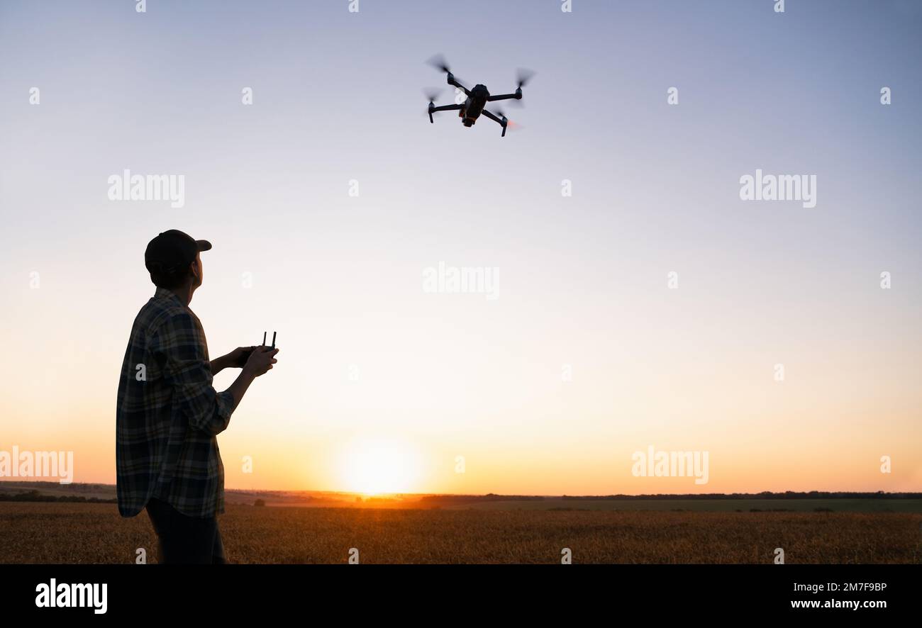Farmer controlla l'irroratrice di droni con un tablet al tramonto. Agricoltura intelligente e agricoltura di precisione Foto Stock