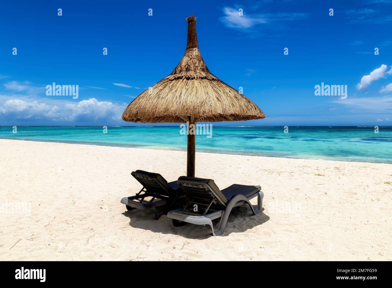 Spiaggia di sabbia bianca e soleggiata con ombrellone di paglia e sedie a sdraio e mare tropicale in un resort tropicale Foto Stock