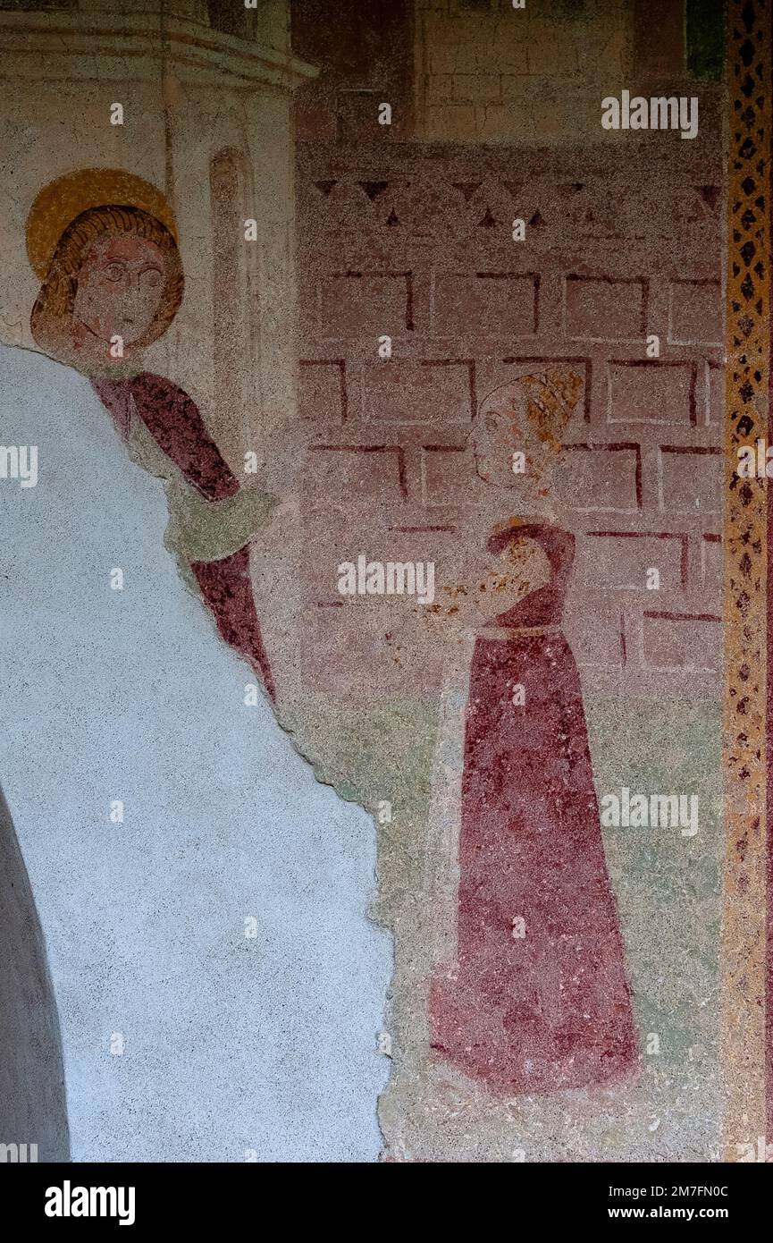 Una donna con accatastati, acconciature in stile alveare, braccia piegate, listato ad un giovane con un alone d'oro in seguito per essere canonizzato come l'eremita sant'Antonio l'Abate o Antonio il Grande. Affresco rustico danneggiato alla fine del 1400s, attribuito all'artista itinerante lombardo Dionisio Baschenis, sulla parete esterna della Chiesa di Sant'Antonio Abate a Pelugo, Trentino-Alto Adige, Italia. Foto Stock