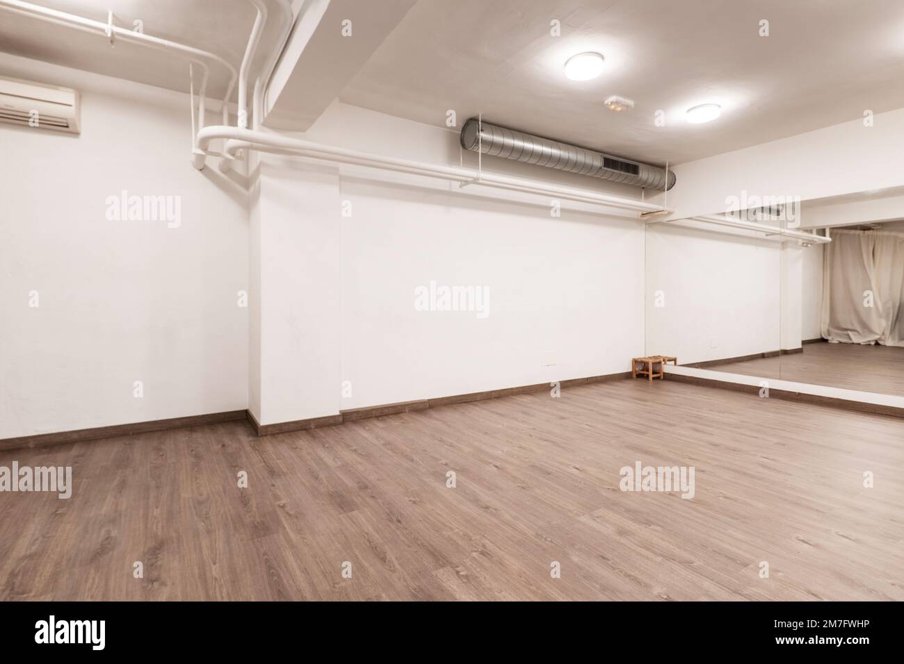 sala da ballo vuota con pavimento in legno, parete coperta da specchi e aria condizionata e tubi di riscaldamento appesi al soffitto Foto Stock