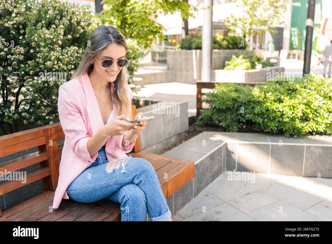 Giovane donna sorridente che usa lo smartphone fuori dal centro commerciale. Dipendenza da Internet e dai social media Foto Stock
